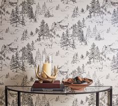 a table topped with a bowl of fruit next to a wallpaper covered in pine trees