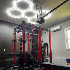 a home gym with red and black equipment in the middle of an empty room that has hexagonal lights above it