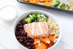 a white bowl filled with beans, broccoli and salmon next to a container of ranch dressing