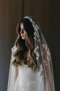 a woman wearing a wedding veil with flowers on the side and long hair in front