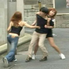 two young women are dancing on the street while another woman is walking behind them with her arms around each other