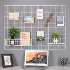 a laptop computer sitting on top of a desk next to a white wire wall hanging