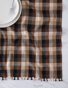 a white plate and fork sitting on top of a brown checkered table cloth with tassels