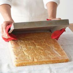 a person is using a knife to cut bread on a sheet of paper with red mitts