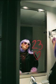 a woman with purple hair is looking at herself in the mirror