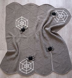 two black bugs sitting on top of a gray knitted blanket with spider webs