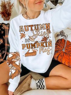 a woman sitting on top of a bed wearing a white shirt with autumn pies and pumpkin pies