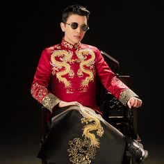 a man sitting in a chair wearing a red and gold chinese shirt with dragon embroidery on it