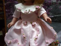 Give your doll a new "pretty pink"  and off white frock  for the holidays .  She'll stand out among the others and continue to give you pleasure dressed in cotton candy pink   with a row of pretty roses winding around the overskirt.  The shapely collar  complete with satin rosebuds ,is in contrast as is the underskirt that has a beautiful  woven pattern of flowers and leaves.  Notice the quality of the fabric which goes to make this dress standoial.  Elastic loops around MOP buttons close the back. Off White Frock, Pink Satin Dress For Garden Party, Pink Rose Print Dress For Wedding, Pink Full Gathered Skirt, Satin Frock, Elegant Pink Doll Collar Dress, Vintage Pink Full Skirt, Pink Mini Dress With Ruffles And Doll Collar, Mop Buttons