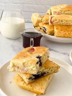 two white plates with biscuits and blueberries on them next to a glass of milk