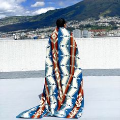 a woman standing on top of a roof covered in a blue and white blanket with mountains in the background