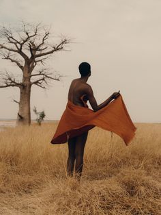 a man standing in the middle of a field holding an orange cloth over his body