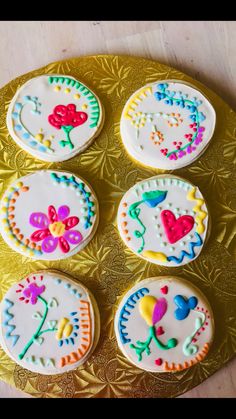 four decorated cookies sitting on top of a gold platter with flowers and hearts painted on them