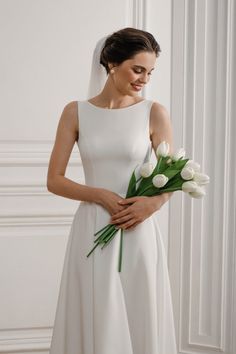 a woman in a white wedding dress holding a bouquet of tulips and greenery