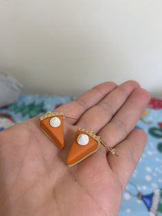 a hand holding two small orange and white triangle shaped earrings with pearls on each ear