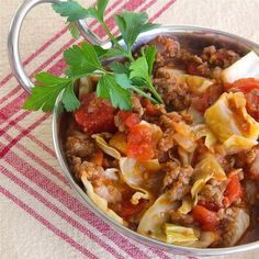 a bowl filled with pasta and meat on top of a red table cloth next to a fork