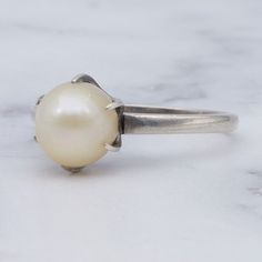 This antique Art Deco sterling silver ring was designed by Mikimoto and features a beautiful 7.5mm pearl in a long six-prong setting. This ring is a size 6 and weighs 2.0 grams. This piece is on great antique condition with light wear and is marked with hallmarks as shown. Classic Pearl Solitaire Rings, Classic Solitaire Pearl Rings, Classic Pearl Drop Ring, Classic Promise Ring With Pearl Drop, Classic Round Rings With Pearl Drop, Timeless Silver Sterling Silver Pearl Ring, Timeless Sterling Silver Pearl Ring In Silver, Timeless Silver Pearl Ring In Sterling Silver, Classic White Gold Ring With Pearl Drop