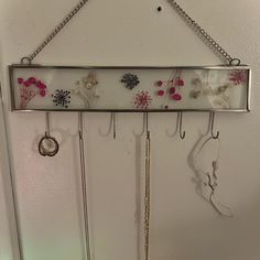 a wall mounted jewelry rack with flowers and chains hanging from it's hooks on the wall