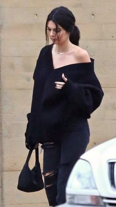 a woman in black sweater and ripped jeans walking down the street with her hand on her hip