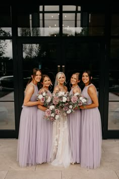 a group of women standing next to each other in front of a glass building holding bouquets