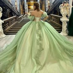 a woman in a green ball gown standing on stairs with her back to the camera