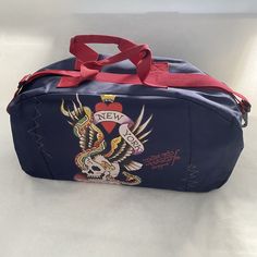 a blue duffle bag with an eagle tattoo design on the front and red straps