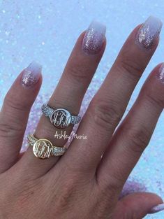 a woman's hand with two rings on it and glittery nails in the background