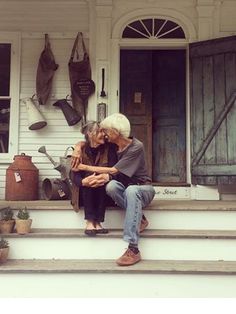 an older couple sitting on the front steps of a house with their arms around each other