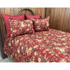 a bed with red and green floral bedspread on top of wooden headboard