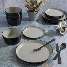 a table set with black and white plates, silverware and flower vase on it