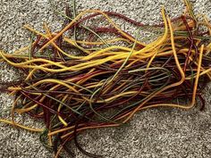 some yellow and red yarn is laying on the ground with it's ends curled up