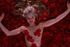 a woman with her arms spread out in the air surrounded by red roses and petals