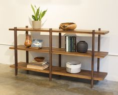 a wooden shelf with books, vases and other items on it next to a white wall