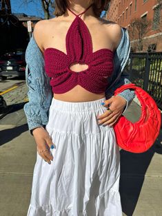 a woman standing on the sidewalk wearing a white skirt and crop top with a red purse