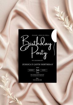 a black and white birthday party card on top of a pink satin background with leaves