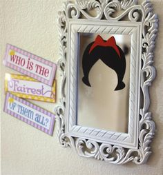 a white frame with a red bow hanging on the wall next to a sign that says who is the fairest of them all?