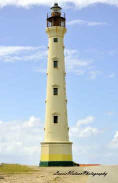 a white and yellow light house sitting on top of a sandy beach