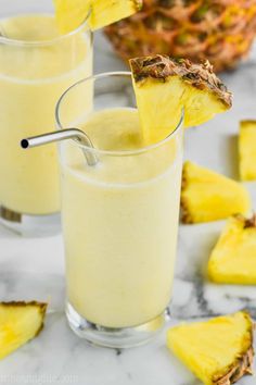 two glasses filled with pineapple smoothie next to sliced pineapples on the table