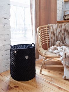 a black basket sitting on top of a wooden floor next to a chair and window