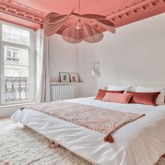 a white bed sitting under a pink painted ceiling in a bedroom next to a window