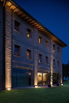 a large building that is lit up at night with lights on the windows and grass in front of it