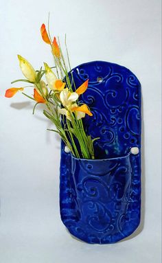 a blue vase with flowers in it sitting on a white surface next to a wall