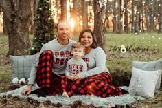 a man and woman are sitting on a blanket in the woods with their baby boy