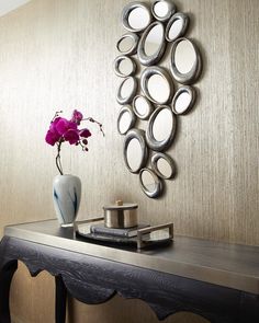 a table with a vase and some flowers on it next to a wall mounted mirror