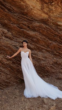 a woman standing in front of a rock formation wearing a white dress and holding her hand out