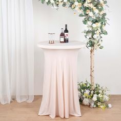 a table with flowers and bottles on it next to a white curtained wall in the background