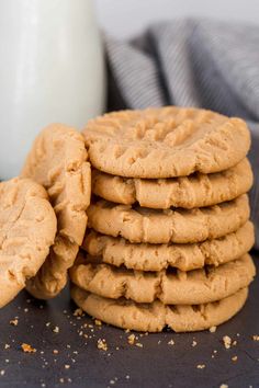 a stack of peanut butter cookies next to a glass of milk on a black surface