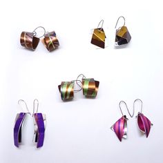 six different colored earrings are arranged on a white surface and one is in the shape of an origami