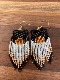 two pairs of beaded earrings with black, white and orange beads on wooden surface