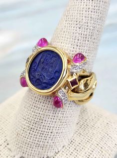 Unique Vintage Italian ring featuring lapis, rubies, tourmalines and diamonds set in an 18k gold chain link setting *12.80x 11.3 hand carved lapis lazuli intaglio (shield) *Cuban style link chain 11mm *US size 8.5 *Pink tourmalines cabochons set on corners of bridge with white diamonds pave set along side ~0.16carats *Two square cut rubies bezel set *15.8 grams *Made in Florence, Italy Circa 1970s Italian Ring, Chain Link Ring, Cuban Style, Link Ring, 18k Gold Chain, Diamond Choker, Linking Rings, Blue Band, Square Cut